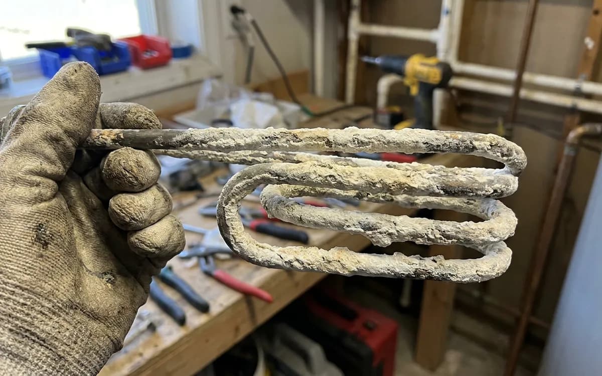 Scale and sediment residue on a drained water heater element held in a gloved hand